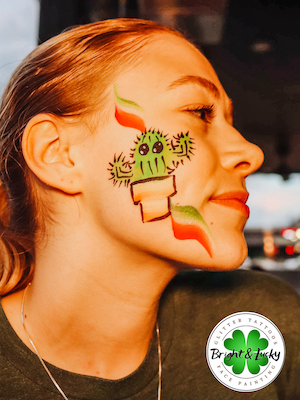 Smiling face with a custom face paint design: cactus cheek.