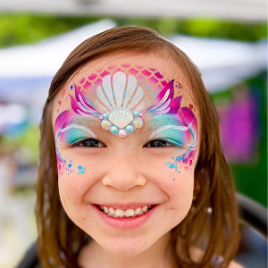 Little girl with a mermaid face paint design on her forehead and a cluster of gems in the center between her eyebrows.